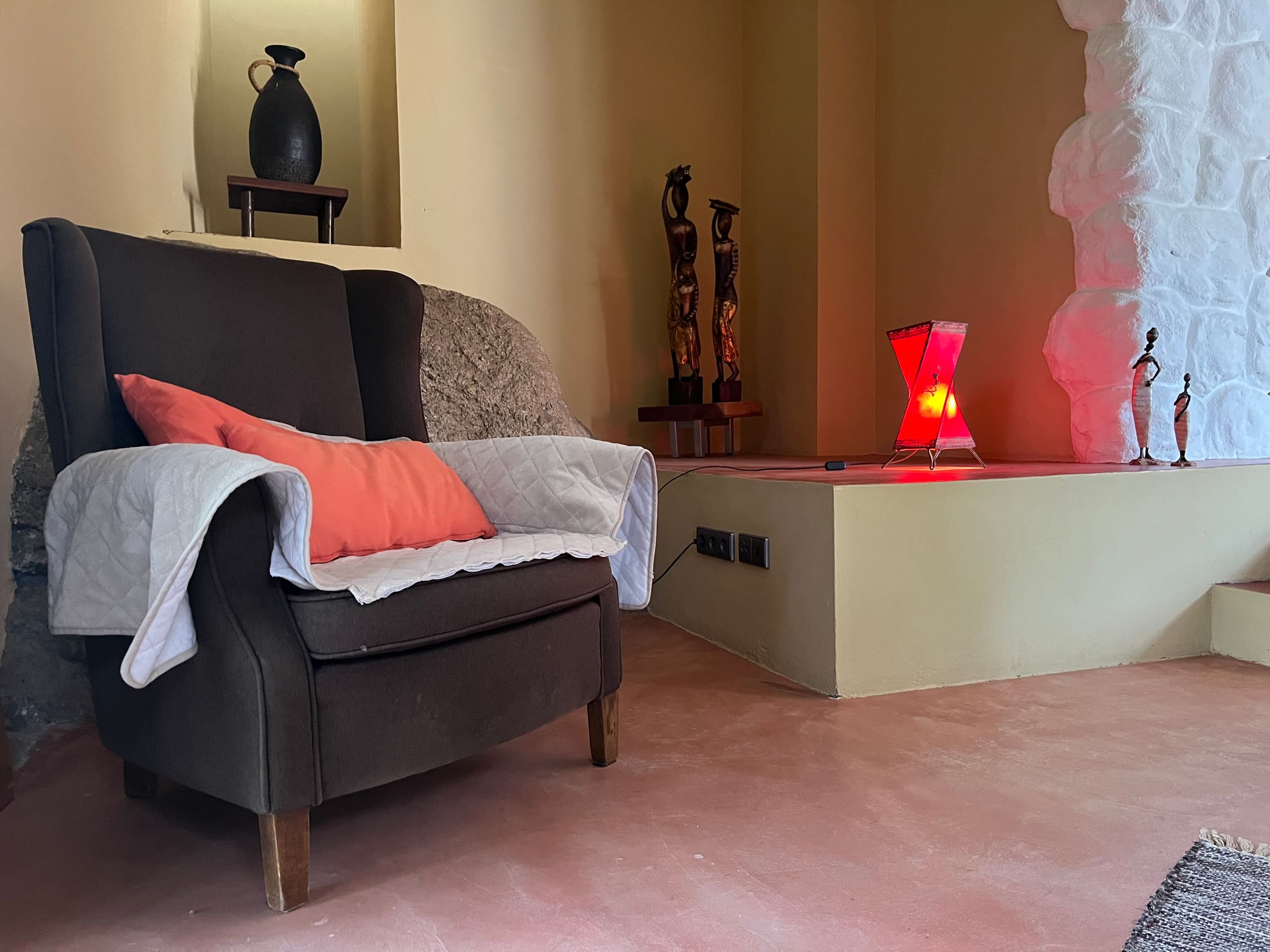 Gemütliche Sitzecke mit dunklem Sessel, Kissen, Deko-Figuren und roter Stimmungsleuchte.