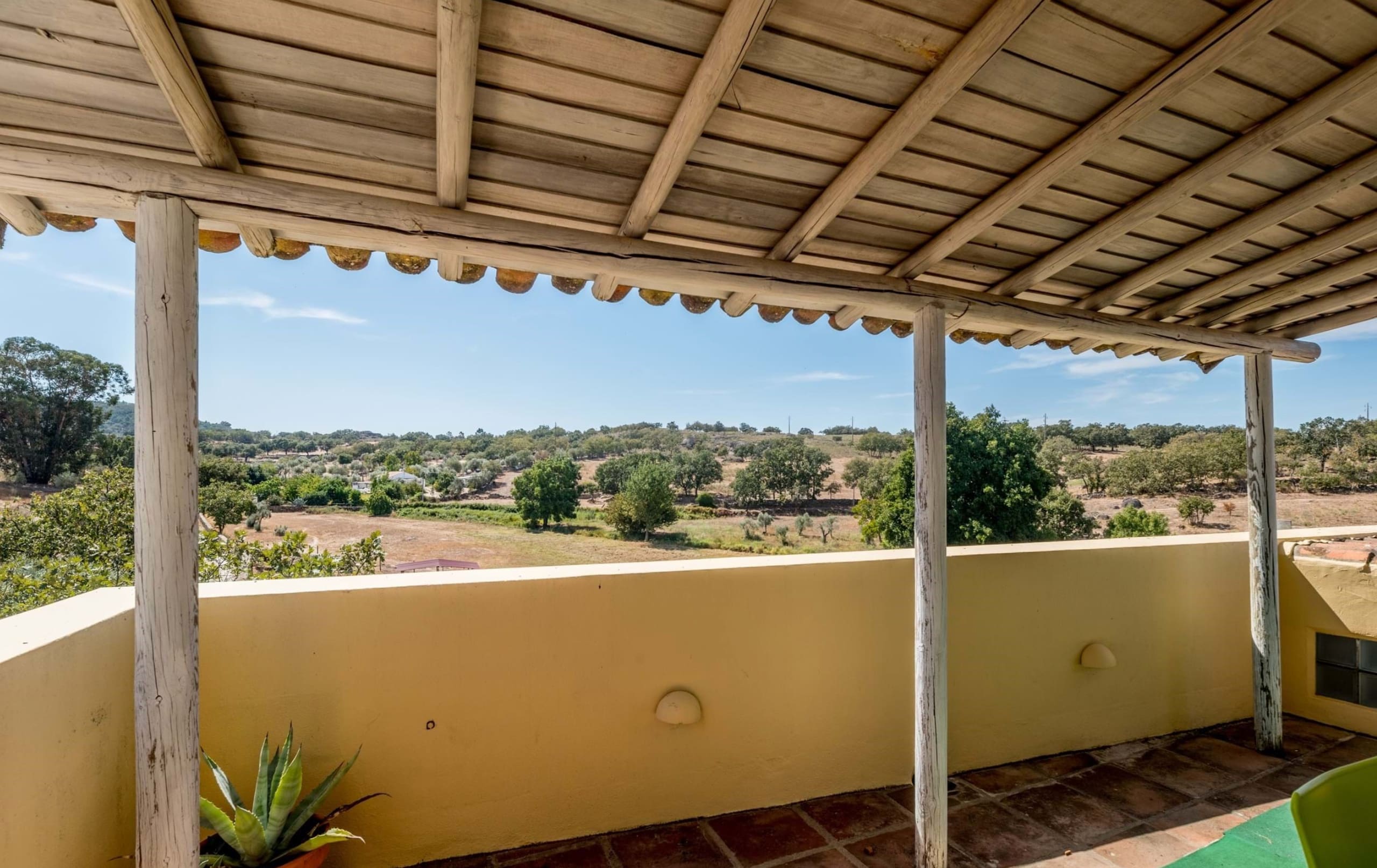 Überdachte Terrasse mit Holzbalken und Blick über hügelige Landschaft.