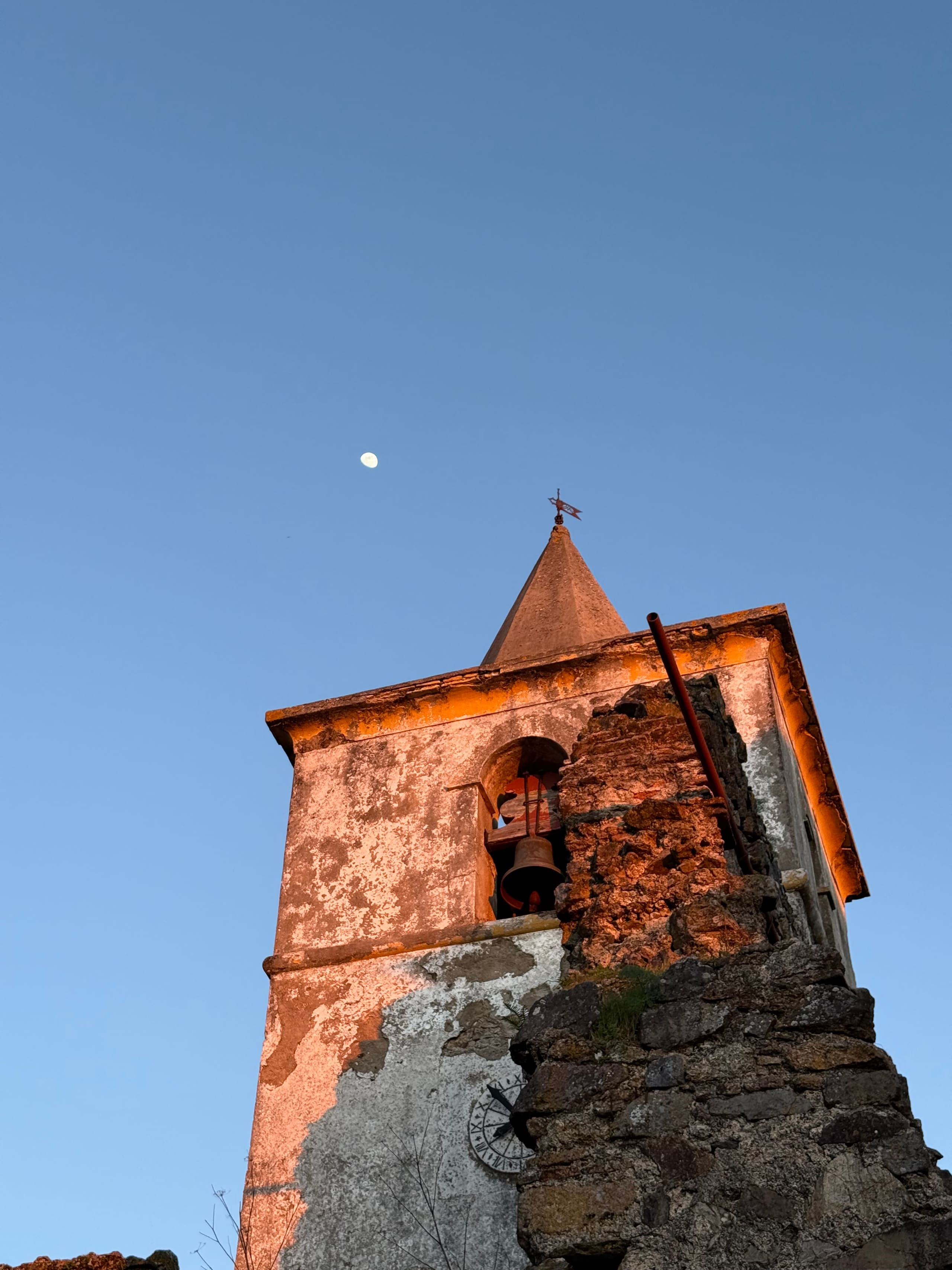 Alter Glockenturm im Abendlicht mit Mond am klaren blauen Himmel.