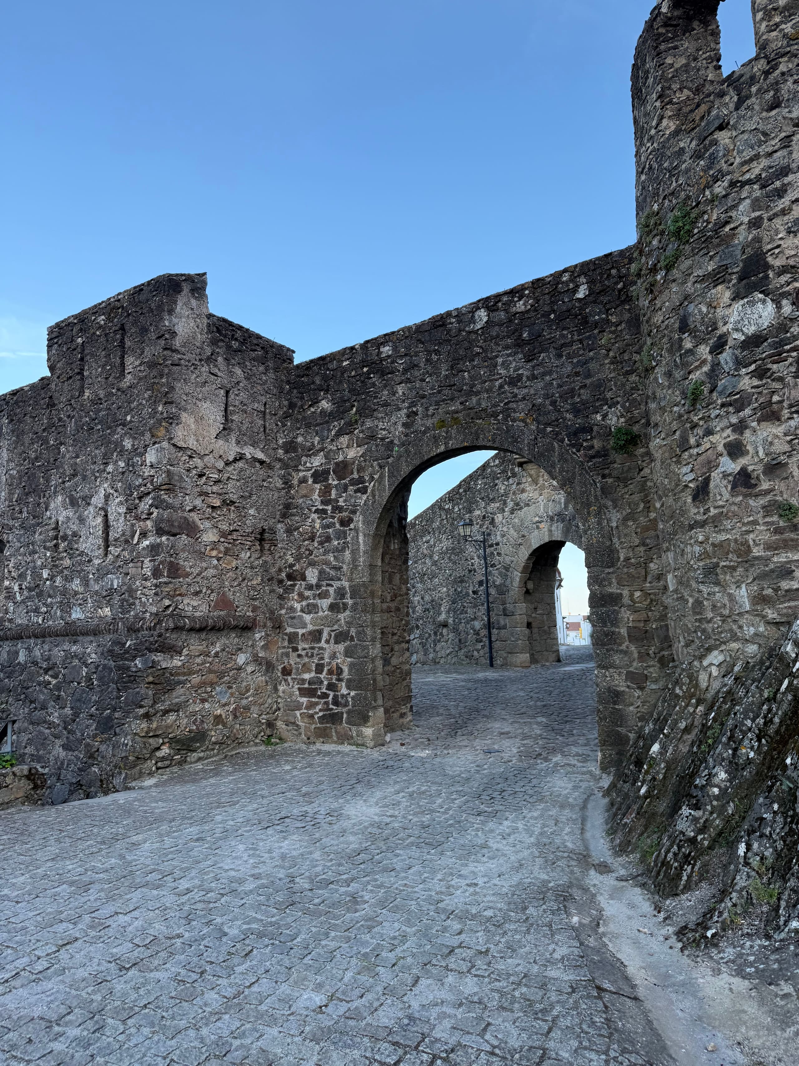 Torbogen einer alten Natursteinmauer über einer gepflasterten Gasse.