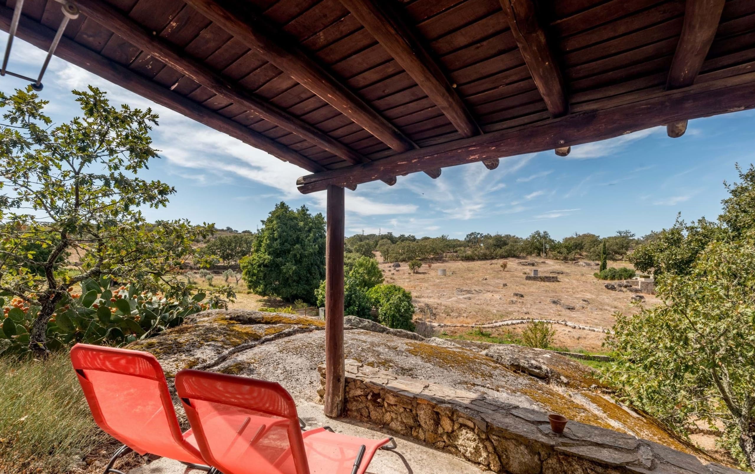 Überdachte Terrasse mit roten Stühlen und Blick über hügelige Landschaft.