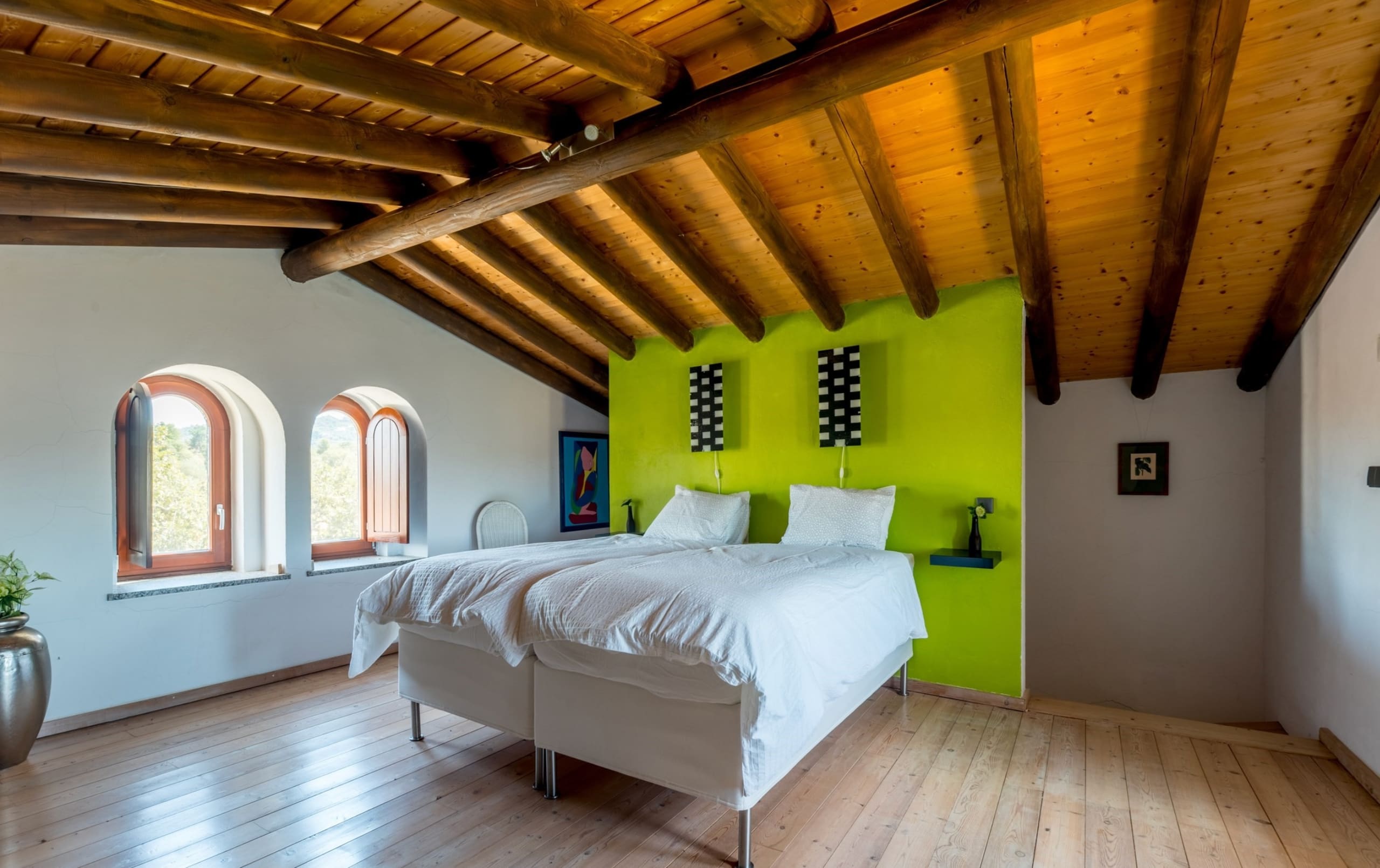 Schlafzimmer mit Holzbalkendecke, grüner Wand und Rundbogenfenstern