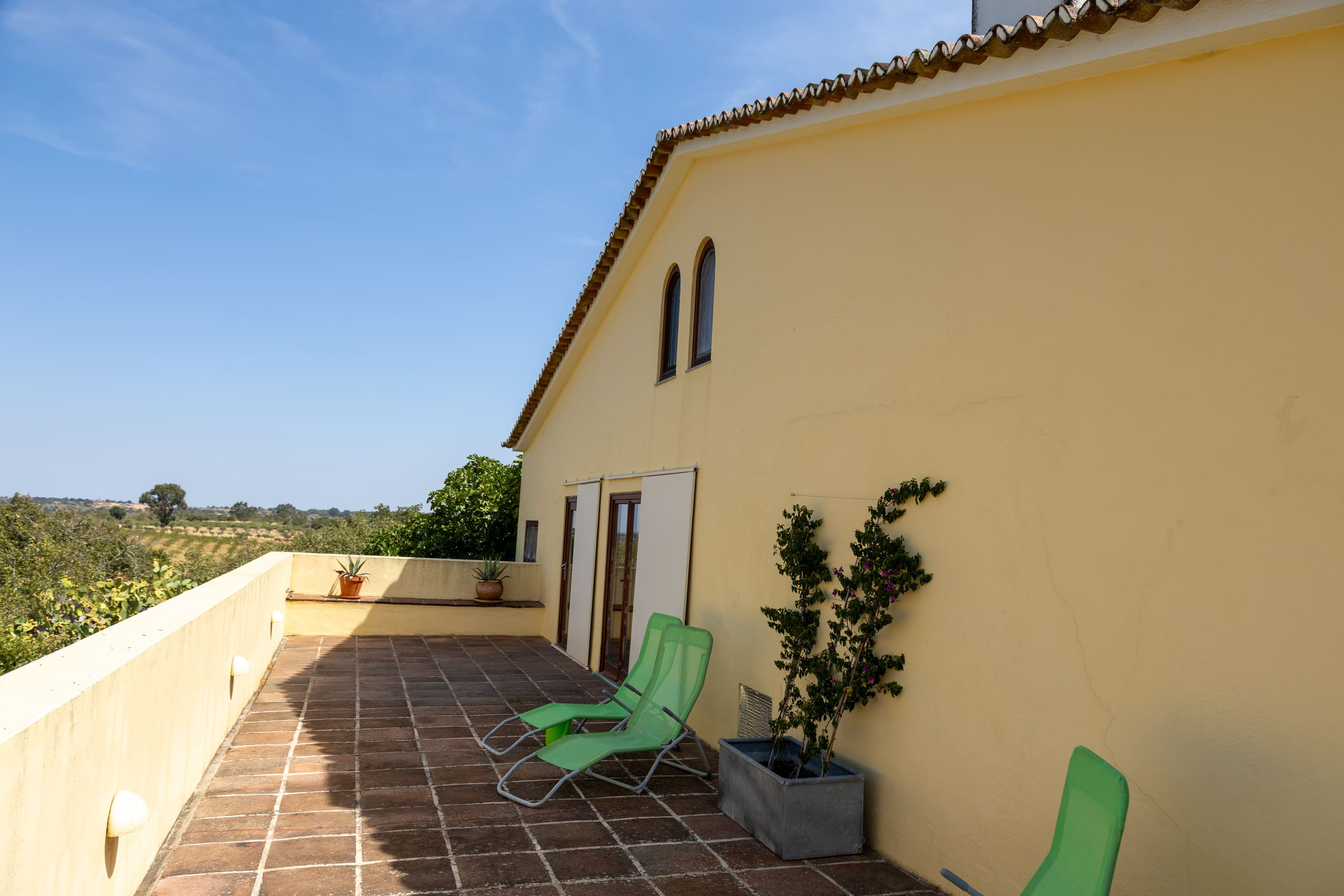 Dachterrasse mit Terrakottafliesen, grünen Liegestühlen und Blick über die Landschaft.