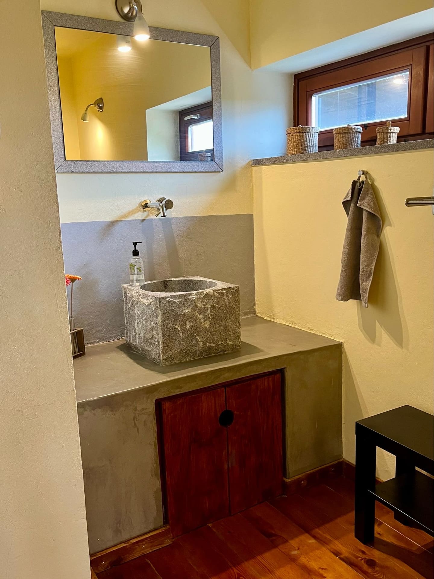 Badezimmer mit quadratischem Natursteinbecken, Spiegel und dunklem Holzschrank.