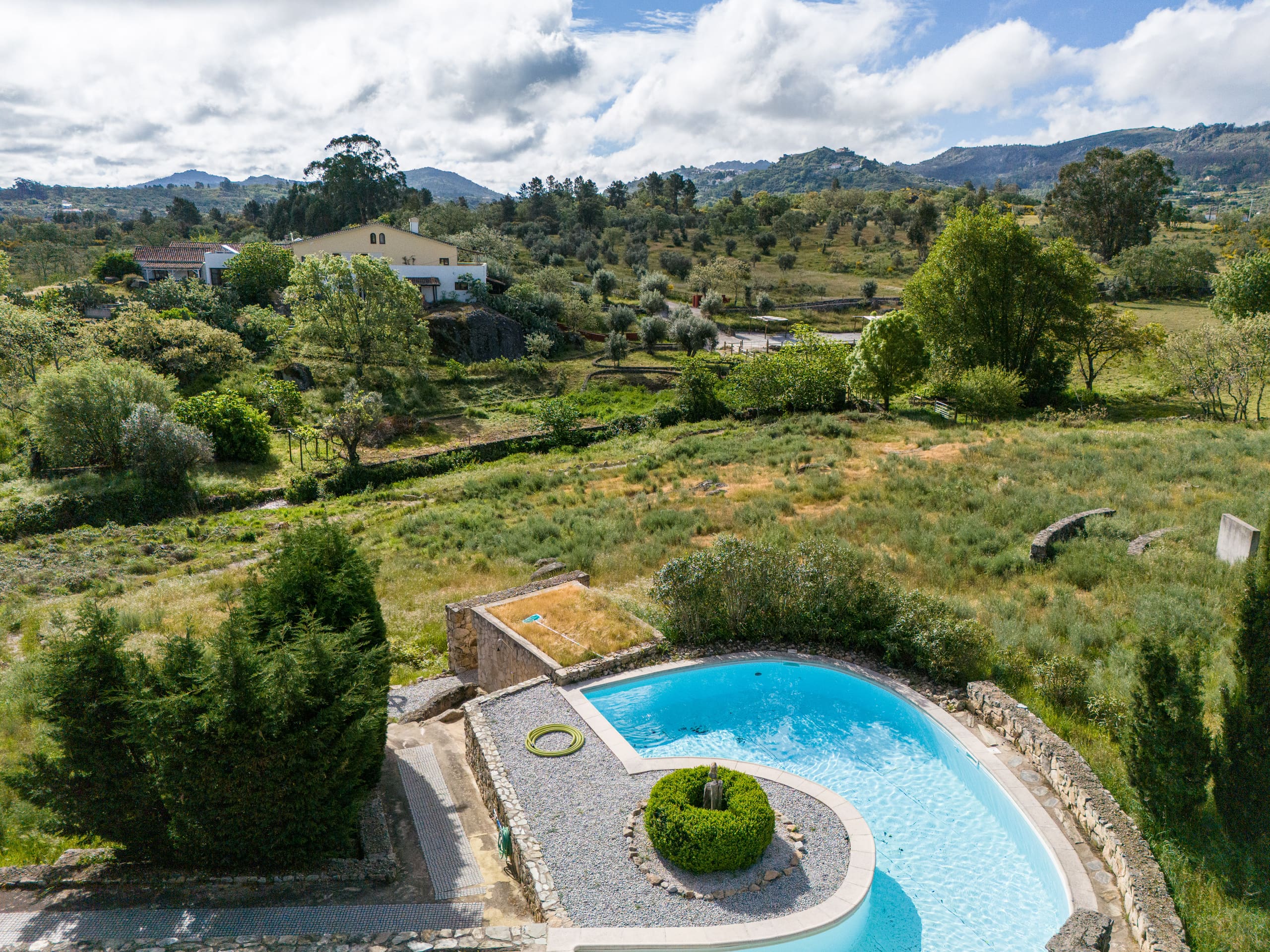 Luftaufnahme eines geschwungenen Pools im Garten mit Blick auf Hügel und Landschaft.