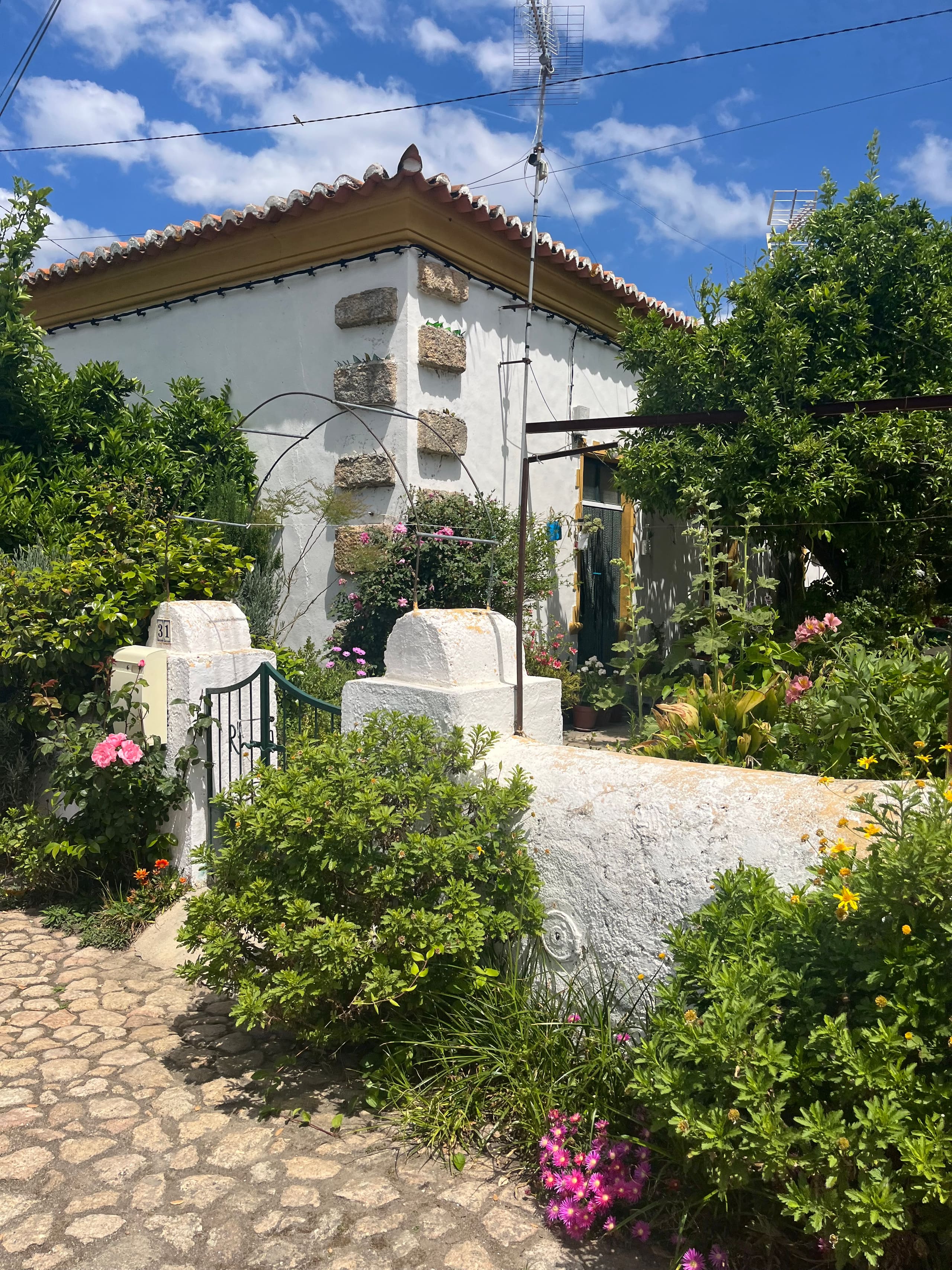 Weiß getünchtes Landhaus mit Ziegeldach hinter blühendem Garten und Steinmäuerchen.