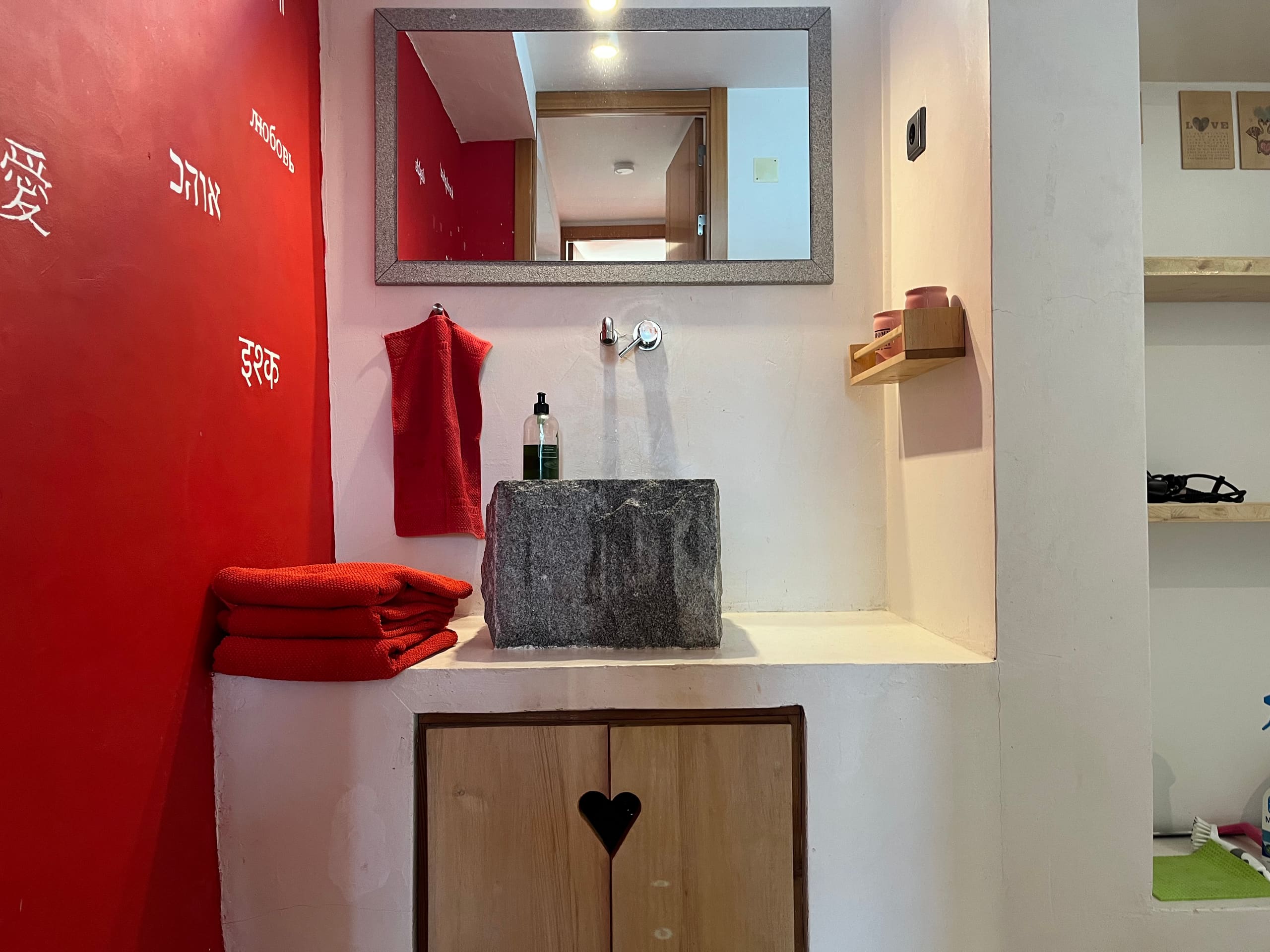 Bad mit roter Wand, Steinwaschbecken, Spiegel und roten Handtüchern.