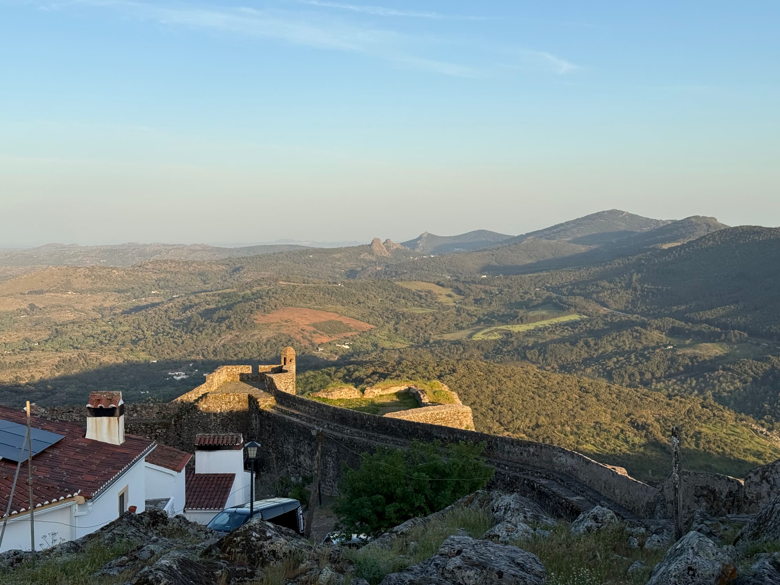 Weiter Blick von einer Burgmauer über hügelige Landschaft bis zu fernen Bergen.