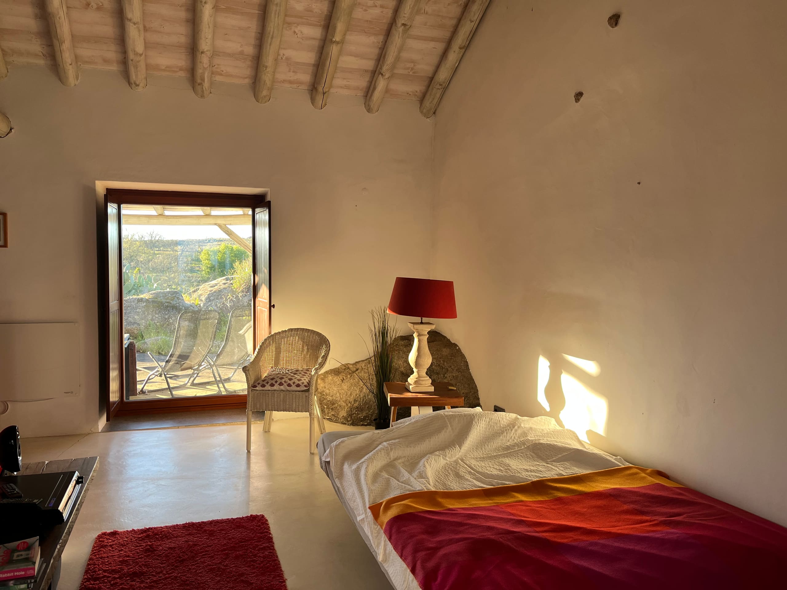 Schlafzimmer mit Terrassentür, Bett mit roter Decke und Korbsessel