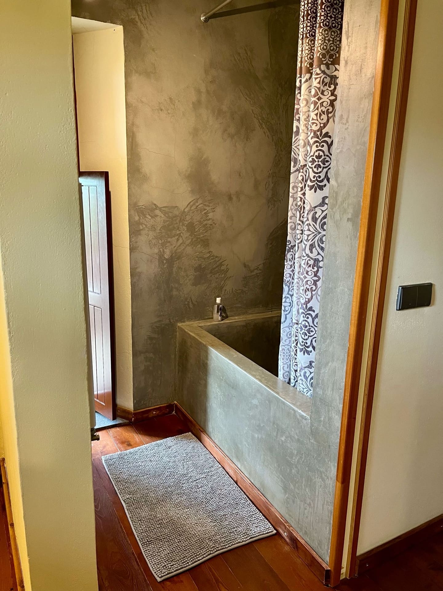 Badezimmer mit gemauerter Badewanne, Duschvorhang und Holzdielenboden