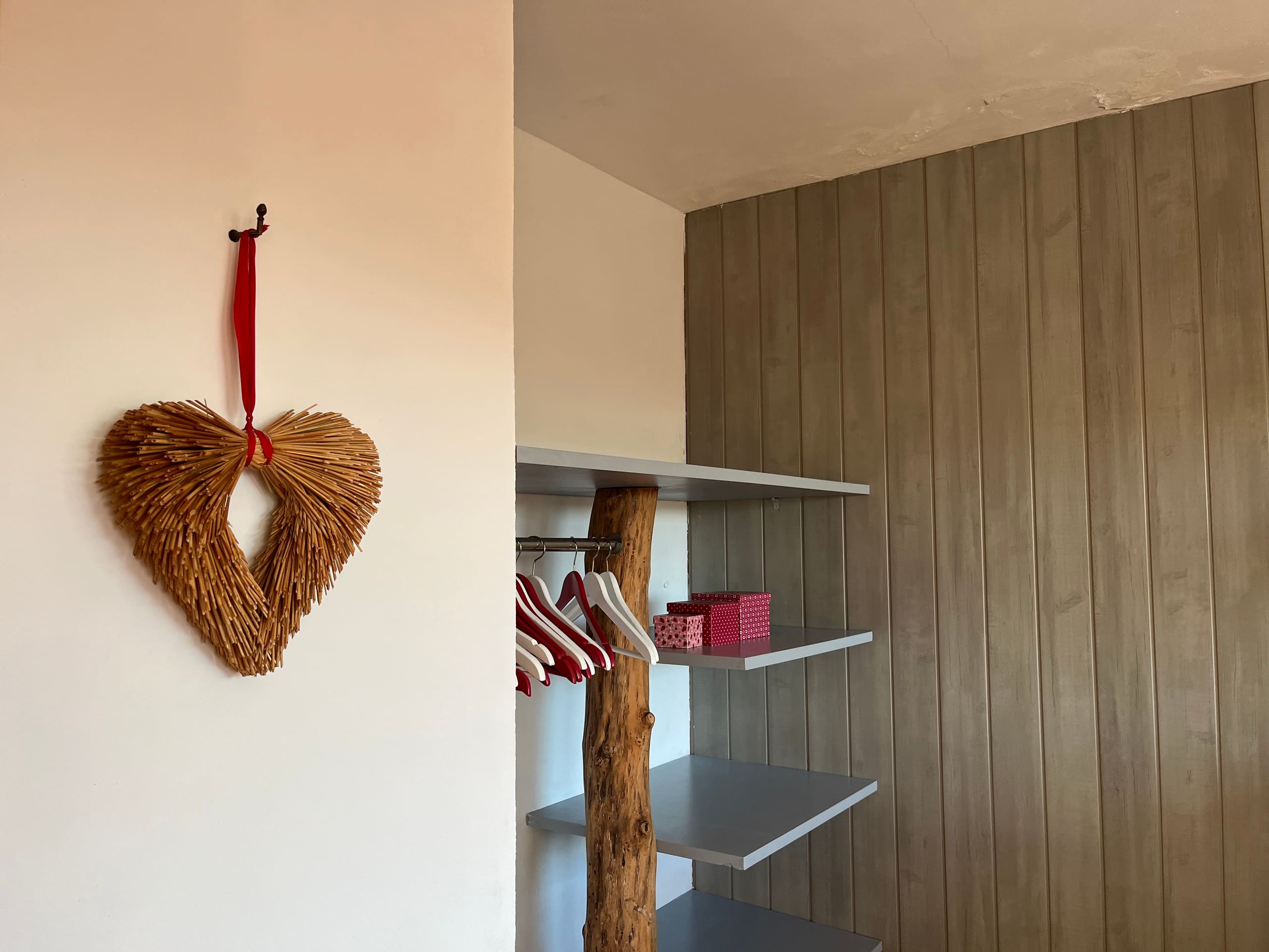 Ankleidebereich mit Kleiderstange, Regalen und dekorativem Stroh-Herz an der Wand
